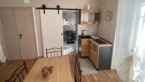 Een kleine keuken met een eethoek, houten kastjes, een spoelbak en een klok aan de muur.