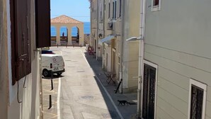 Een smalle straat met gebouwen aan weerszijden, een geparkeerde bus en een helder uitzicht op de zee in de verte.