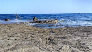 Een rotsachtig strand met een metalen trap die het water in leidt.