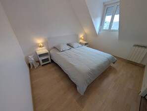 A bedroom with a sloped ceiling, a bed with a striped bedspread, two bedside tables with lamps, and a window with blinds.