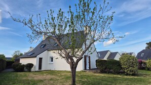 Ein Haus mit schrägem Dach, einem kleinen Garten und einem Baum davor.