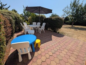 An outdoor patio with a table and chairs, a large umbrella, and a brick pathway.