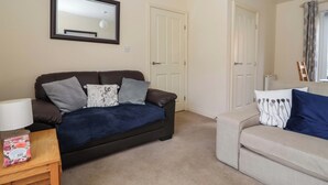 A living room with a dark brown sofa, a beige sofa, a wooden side table, and a mirror on the wall. - Sea Glass Cottage (Filey)