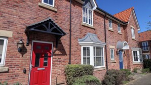 A red door, a white window with shutters, and a blue door on a brick building. - Sea Glass Cottage (Filey)