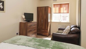 A bedroom with a bed, a TV on a dresser, a wardrobe, a window with blinds, and a radiator. - Sea Glass Cottage (Filey)