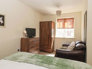 Ein Schlafzimmer mit einem Bett, einem Fernseher auf einer Kommode, einem Kleiderschrank, einem Fenster mit Jalousien und einer Heizung.