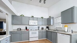 Uma cozinha moderna com armários cinza, fogão branco, micro-ondas e máquina de lavar louça.