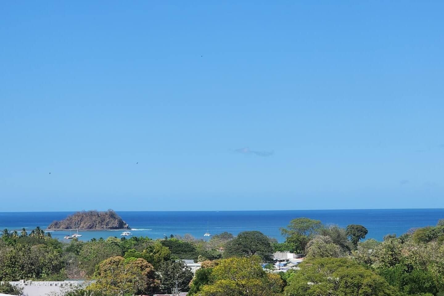 A coastal landscape with a clear sky, a small island, and a few boats in the water.