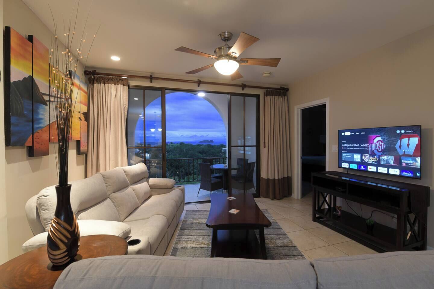 A living room with a sofa, a coffee table, a TV, and a view of the outdoors.