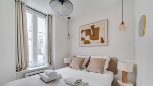 Ein Hotelzimmer mit einem Bett, zwei Nachttischlampen, einem großen abstrakten Gemälde und einem Fenster mit Vorhängen.