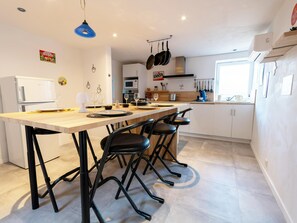 Une cuisine moderne dotée d’un îlot central, de tabourets de bar noirs, d’un porte-ustensiles suspendu et d’un réfrigérateur blanc.