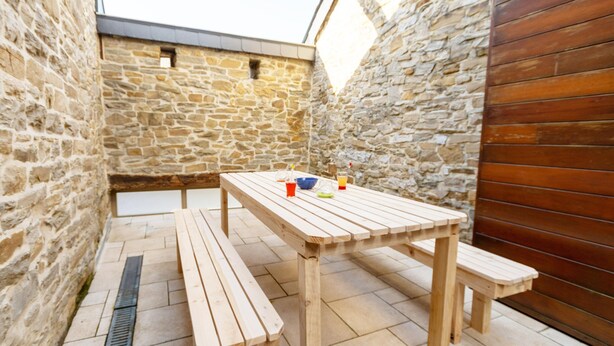 Un patio al aire libre con paredes de piedra, una mesa de madera y bancos.