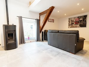 A modern living room with a fireplace, a sofa, a staircase, and a cityscape painting. - Apres la Rando: Ardennes Family Nature Cottage for 6 (Comblain-au-Pont)