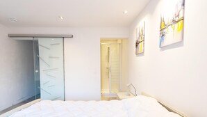 Un dormitorio moderno con cama, vestidor, ducha y un cuadro en la pared.