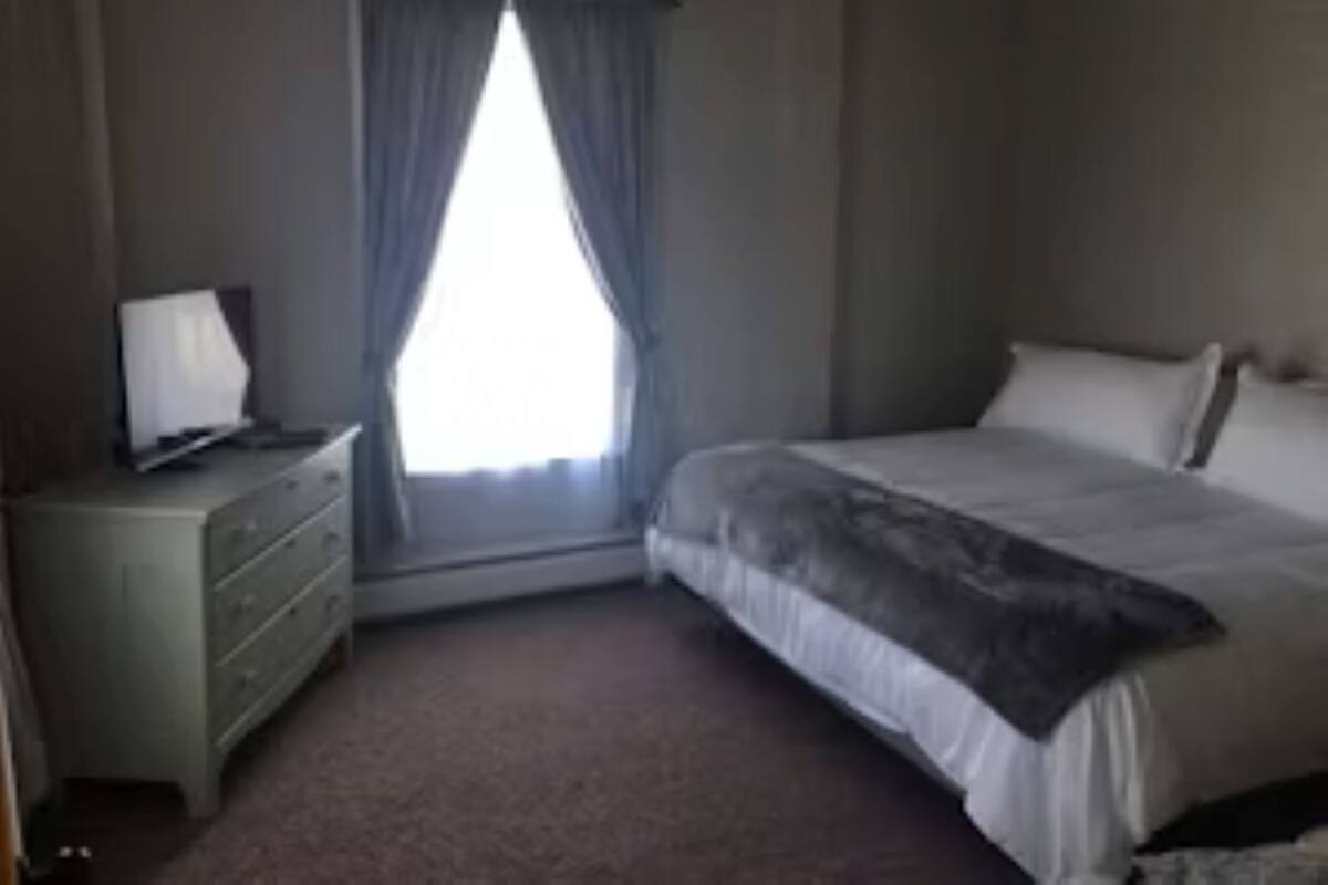 A bedroom with a bed, a dresser, and a window with curtains.