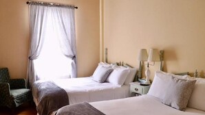 Habitación de hotel con dos camas, una silla, una mesita de noche con lámparas y una ventana con cortinas.
