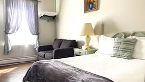 Una habitación de hotel con una cama, una mesita de noche, una lámpara, una ventana con cortinas y un cuadro en la pared.