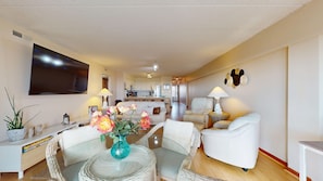 A living room with a TV, a dining area with a table and chairs, a kitchen in the background, and a sofa. - Waters Edge - A 3 bedroom, 2 bathroom, condo located right on the beach! (Brigantine)