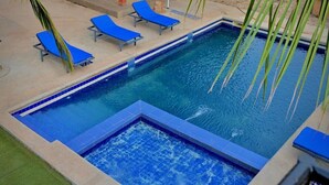 A rectangular pool with a blue tiled edge, surrounded by lounge chairs and palm trees. - la villa du parc (Niaga)