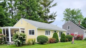 A two-story house with a porch, surrounded by well-maintained lawns and trees. - Charming 2-bedroom house in peaceful Ogunquit with AC and screened porch. (Ogunquit)