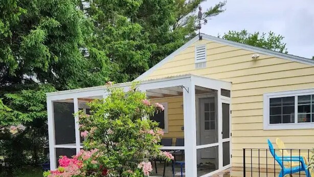 A single-story yellow house with a covered porch and a small garden area with stepping stones leading to the entrance. - Charming 2-bedroom house in peaceful Ogunquit with AC and screened porch. (Ogunquit)