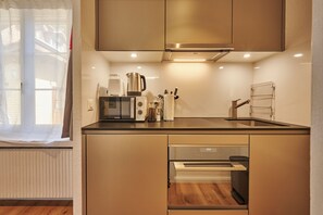 Une cuisine moderne dotée d’appareils électroménagers intégrés, d’une fenêtre ornée de rideaux légers et d’un plancher en bois.