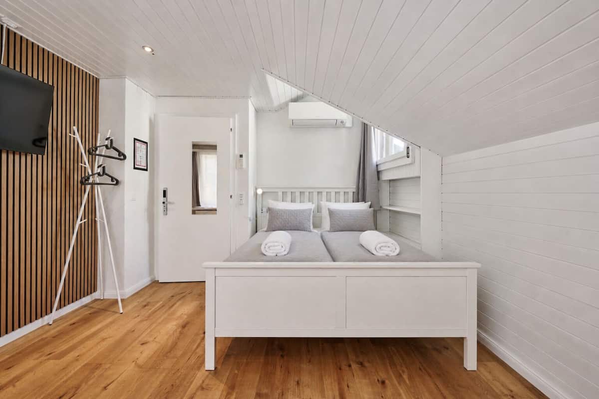 A bedroom with a white bed, wooden floor, and a sloped ceiling.