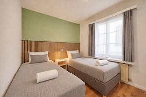 Une chambre d’hôtel avec deux lits, une fenêtre avec des rideaux, une table de chevet avec une lampe et un mur d’accent vert.