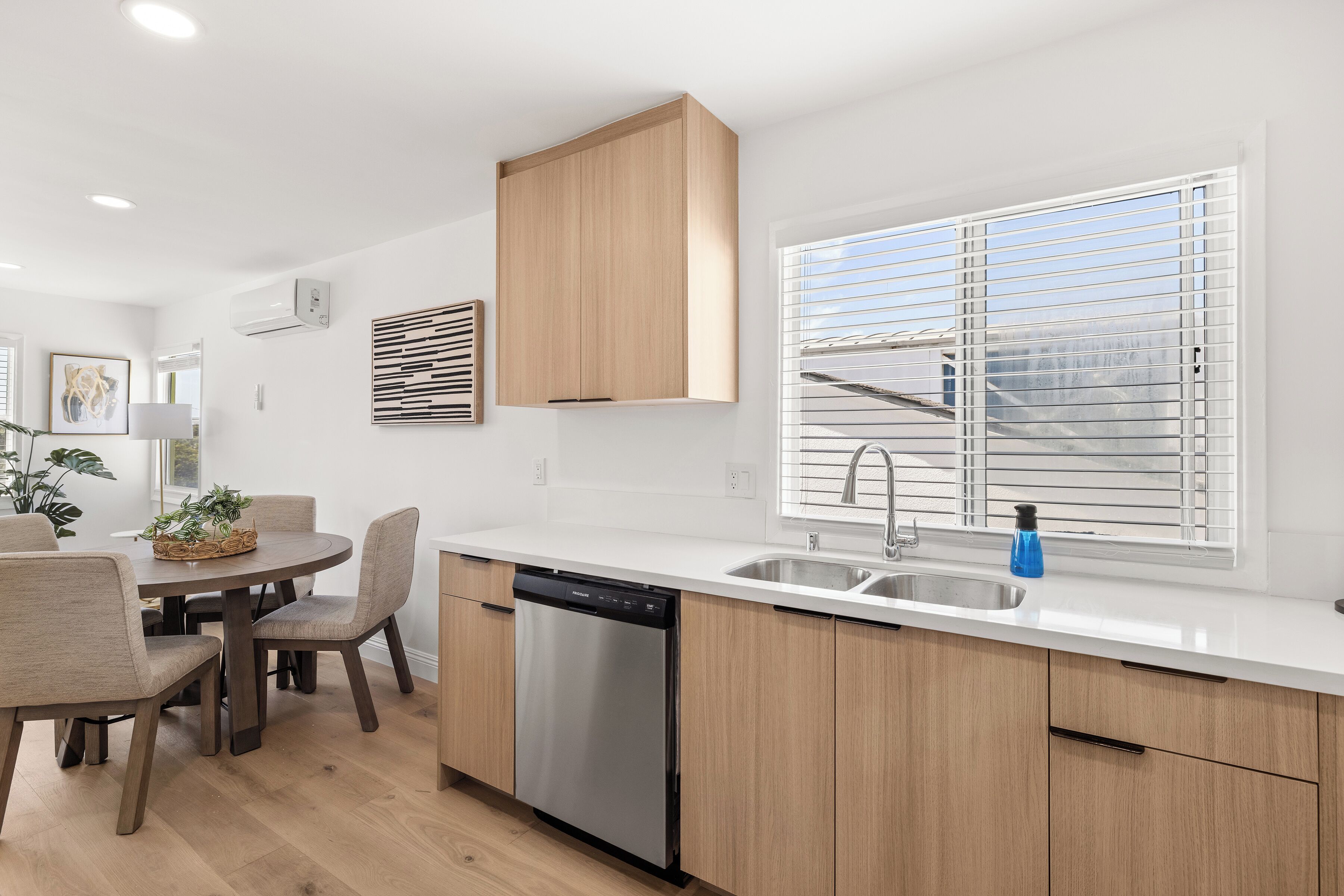 A modern kitchen with a dishwasher, wooden cabinets, a sink, and a window with blinds.