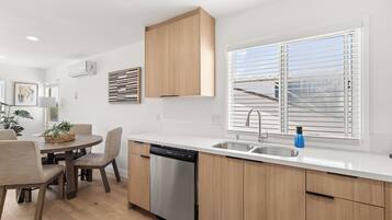 A modern kitchen with a dishwasher, wooden cabinets, a sink, and a window with blinds.