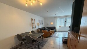 Un salon moderne comprenant un coin repas, un canapé, un téléviseur et un meuble en bois.