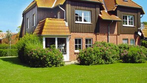 Une maison à deux étages, avec une façade en briques, de nombreuses fenêtres et un toit en pente.
