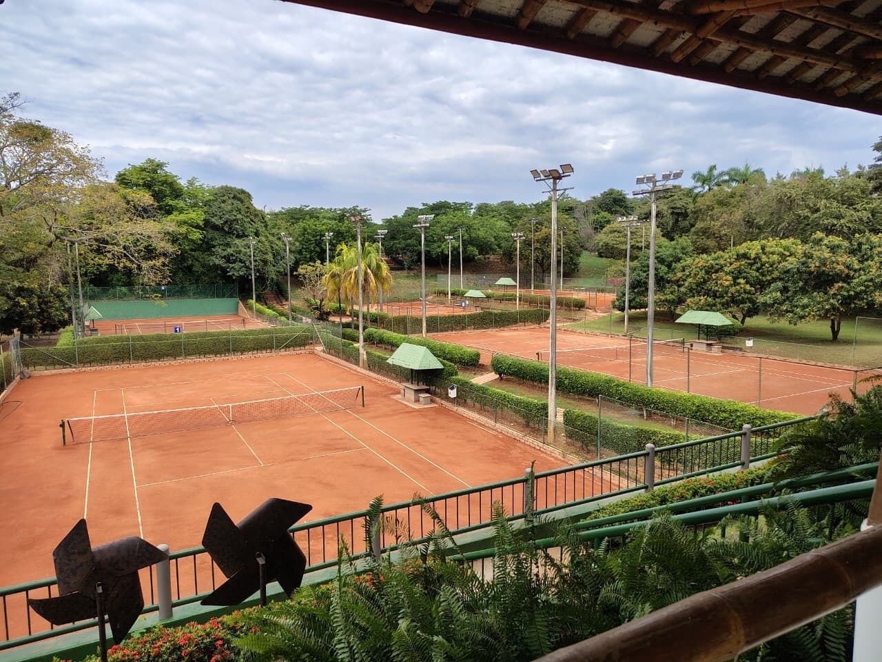 A tennis court with surrounding greenery and a covered seating area.