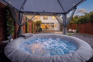 A hot tub under a tent with a house in the background.