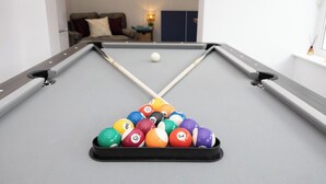 Et billardbord med kugler arrangeret i en trekant, en kø og en sofa i baggrunden.