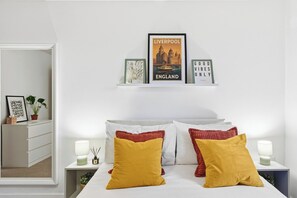 Een slaapkamer met een bed, bedlampen, een spiegel, een dressoir en wanddecoratie, waaronder een ingelijste poster en een bord.