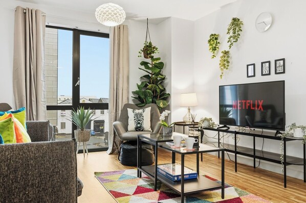 A modern living room with a sofa, armchair, coffee table, and a TV displaying 'NETFLIX'. - Luxury 2BR | Baltic Triangle & Sefton Park (Merseyside)