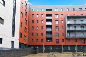 A multi-story building with a red facade, balconies, and a courtyard with benches. - Luxury 2BR | Baltic Triangle & Sefton Park (Merseyside)