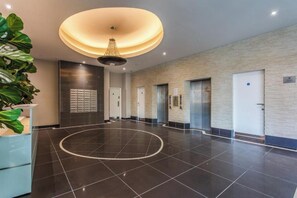 A spacious lobby with a circular floor design, a modern chandelier, and a reception desk with a plant. - Luxury 2BR Brighton | Walk to the Lanes + Beach (Brighton and Hove)