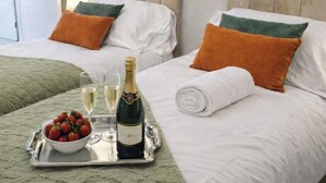 Una cama con almohadas blancas y verdes, una bandeja con champán, copas y un cuenco de fresas.