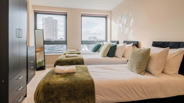 Habitación de hotel con dos camas, un armario y ventanas amplias con vista a la ciudad.