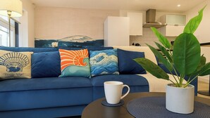 Um sofá azul com almofadas temáticas de ondas, uma caneca branca e um vaso de planta sobre uma mesa redonda.
