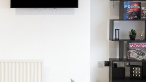 Uma sala de estar moderna com uma televisão de tela plana na parede, uma mesa redonda preta com um vaso de planta e um armário preto com livros e objetos decorativos.