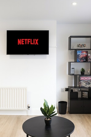 Ein modernes Wohnzimmer mit einem an der Wand montierten Flachbildfernseher, einem runden schwarzen Tisch mit einem Topf und einer schwarzen Kommode mit Büchern und Dekoration.