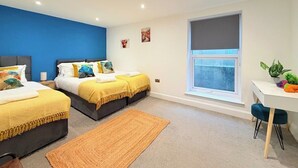 Quarto moderno com duas camas, uma escrivaninha e uma janela.