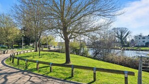 A park with a paved path, a grassy area, and a body of water in the background. - Thamesview | Heathrow | 2 Bed (Staines-upon-Thames)