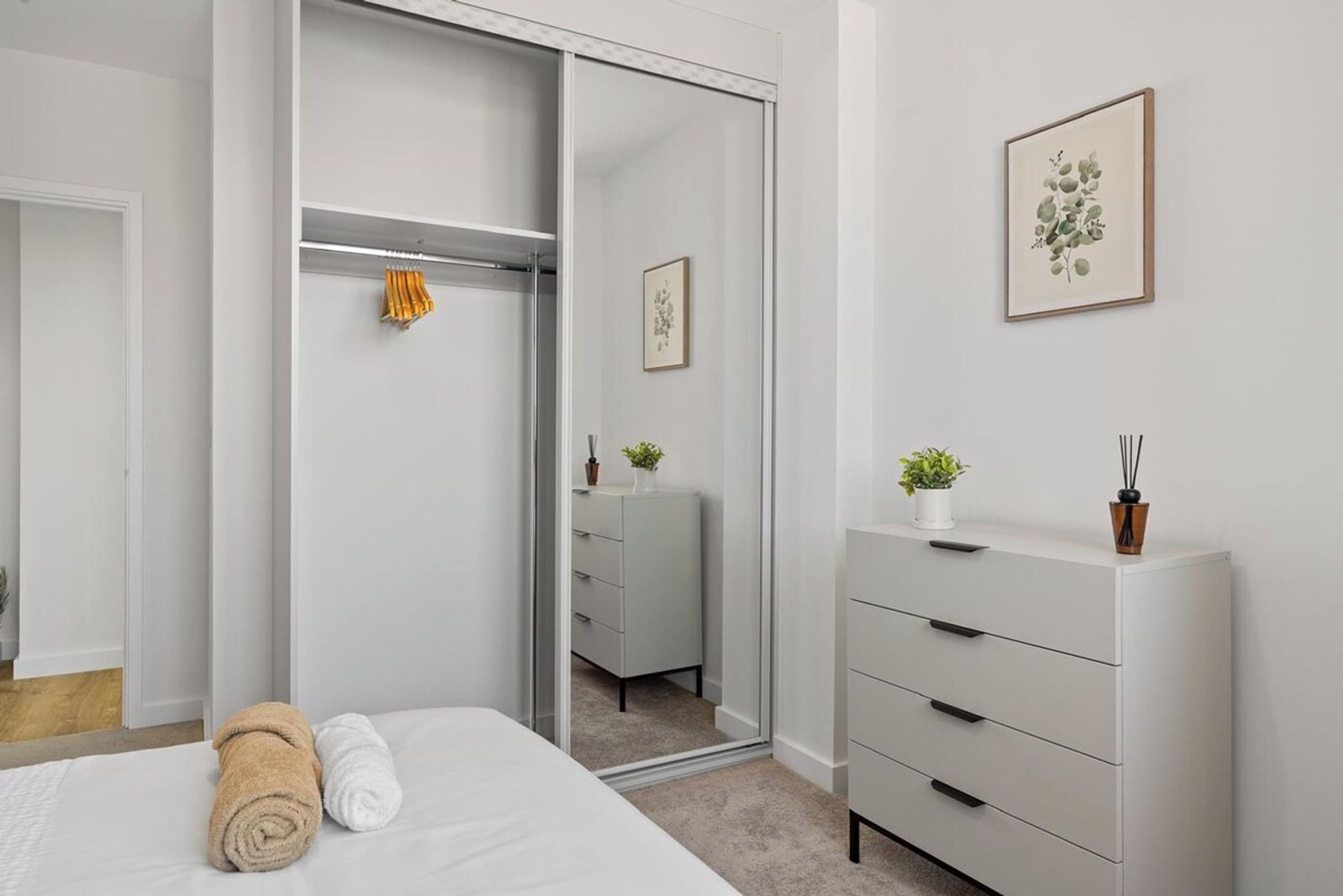 A bedroom with a bed, a wardrobe, a mirror, and a dresser.