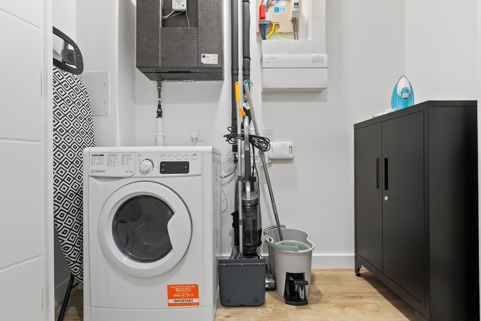 A laundry area with a washing machine, a vacuum cleaner, and a cabinet.