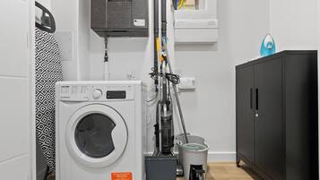 A laundry area with a washing machine, a vacuum cleaner, and a cabinet.