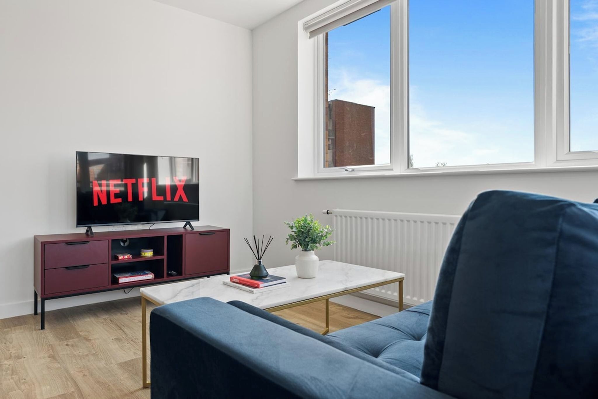 A modern living room with a flat-screen TV, a sofa, a coffee table, and a window with a view.